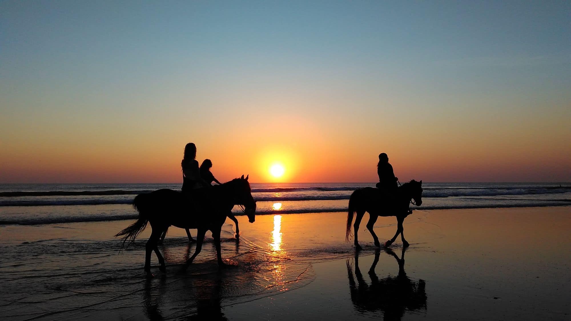 Deux cavaliers au galop sur la plage au coucher du soleil